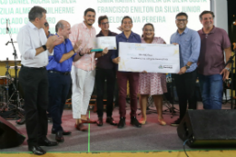 Imagem: foto dos estudantes no palco do evento recebendo um cheque de tamanho grande com o prefeito de Fortaleza ao lado