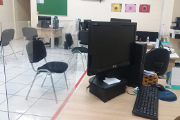 Imagem: foto da sala da Central com foco em uma estrutura de acrílico que separa a mesa de atendimento da pessoa que será atendida