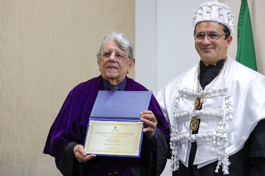 Imagem: Foto mostra o Professor Ernesto Pitombeira, com veste talar, segurando o diploma de 