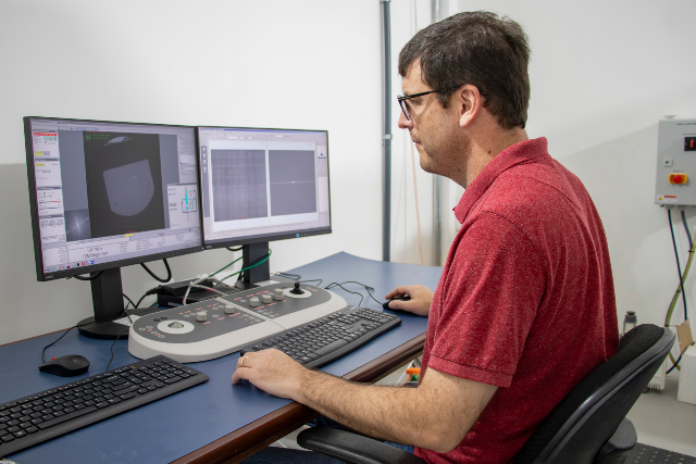 Imagem: Homem branco de camisa vermelha sentado em frente a um computador com dois monitores (Foto: Gutierrez Réges)