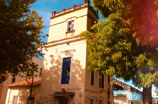 Imagem: foto de uma torre de um prédio amarelo com alguns grafites e pixações na parede