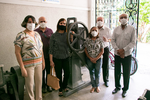 Imagem: A diretora da Farmácia-Escola, Cristiani Lopes; os titulares da PROPLAD e da PREX, Prof. Almir Bittencourt e Profª Elisabeth Daher, respectivamente; a farmacêutica Socorro Vieira; o reitor da UFC, Prof. Cândido Albuquerque; e o vice-reitor, Prof. Glauco Lobo, com a máquina pica-pau de compressão, que produzia comprimidos até o fim da década de 1970 (Foto: Ribamar Neto/UFC Informa)