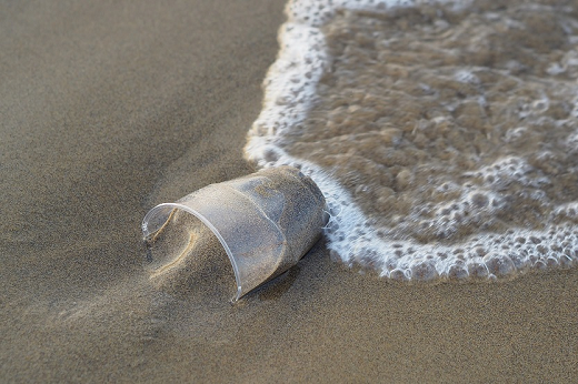 Copo de plástico jogado na areia da praia, com água do mar o molhando