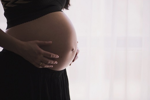 Close em barriga de uma mulher grávida; ela põe as mãos sobre a barriga