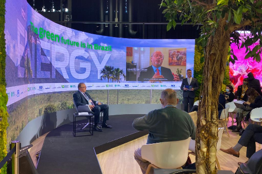 Imagem: foto do local de apresentação na COP26, com um telão onde aparece vídeo do reitor Cândido Albuquerque