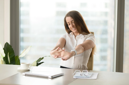 Imagem: mulher sentada e esticando os braços em frente a uma mesa com notebook