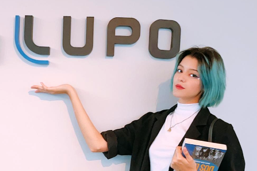 Imagem: Melanie Lopes posa em frente ao logotipo da Lupo