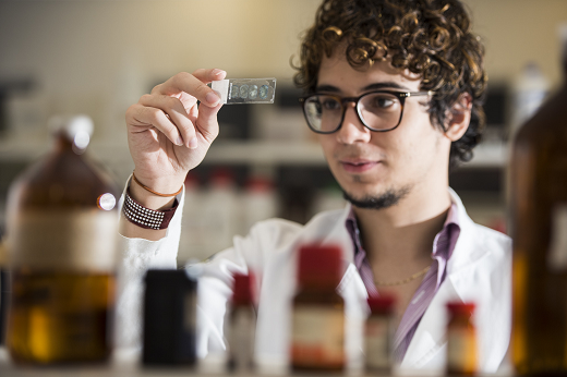 Imagem: Jovem estudante branco, de óculos, segura nas mãos lâmina transparente em laboratório. (Foto: Jr. Panela/ UFC Informa) 