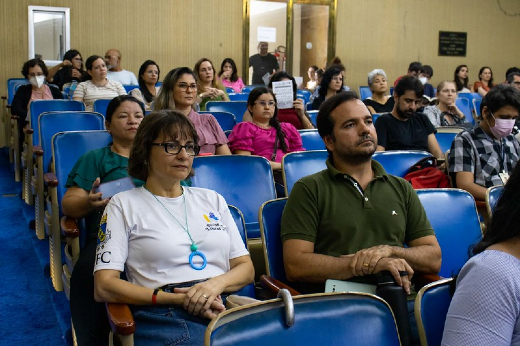 Imagem: publico sentado em cadeiras azuis em ambiente de auditório