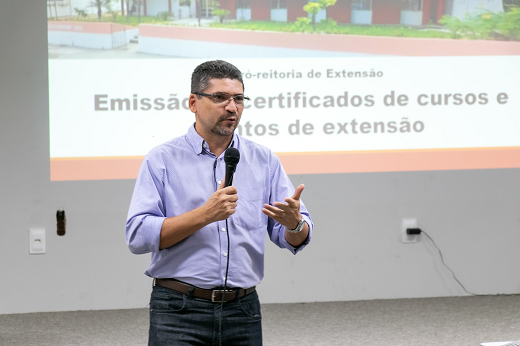 Imagem: homem branco de camisa social azul apresenta slides numa reunião