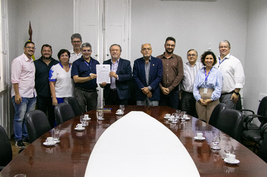 Imagem: grupo de pessoas posam para foto em frente a uma mesa oval