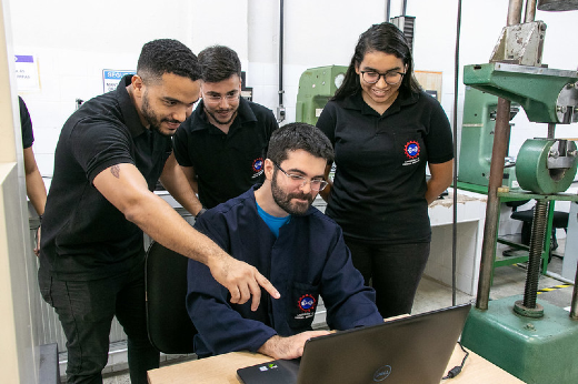 Imagem: quatro pessoas em volta de um laptop analisando dados em laboratório