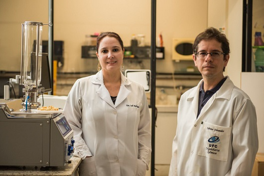 Imagem: A Profª Sueli Rodrigues e o Prof. Fabiano Fernandes lado a lado. Ambos usam jalecos brancos e estão em um laboratório