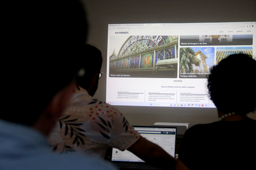 Imagem: sombras de pessoas vendo apresentação em sala escura