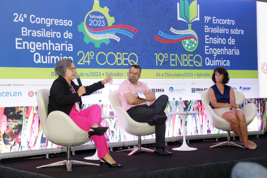 Imagem: três pessoas sentadas em cima de um palco conversam