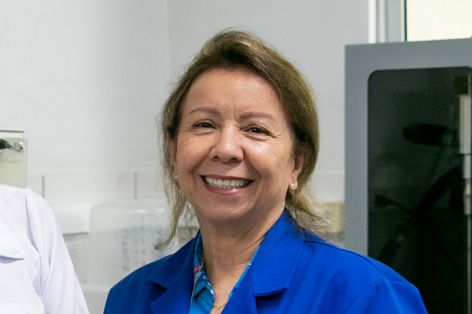 Imagem: Profª Nágila Ricardo, uma mulher loira, de pele branca bronzeada, usando um jaleco azul