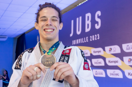 Imagem: aluno-atleta com quimono exibe medalha de ouro