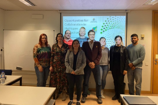 Pesquisadores posam lado a lado em uma das salas do Instituto de Tecnologia Química e Biológica António Xavier, em frente à imagem de um projetor