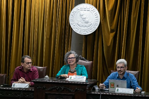 Imagem: O chefe de gabinete, Almir Holanda, a vice-reitora, Diana Azevedo, e o titular da STI, Miguel Franklin, sentados lado a lado, durante reunião do CATI (Foto: Viktor Braga/UFC)