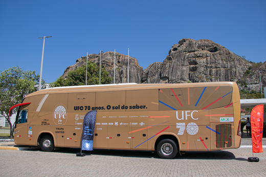 Imagem: Vista lateral do ônibus da Caravana UFC 70 Anos (na cor dourado) que está percorrendo os sertões. Ao fundo, os monólitos de Quixadá