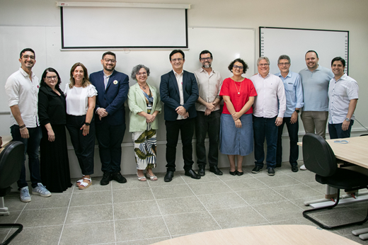 Imagem: De pé, na sede do LAPPELE, estão a visitante espanhola, o reitor e a vice-reitora, ladeados por pró-reitores, pró-reitores-adjuntos, diretores de unidades acadêmicas e servidores docentes, técnico-administrativos e estudantes do CH