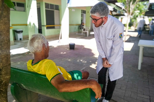 Imagem: estudante de odontologia conversa com idoso sentado em banco