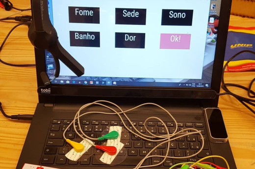 Imagem: laptop ligado mostra diferentes palavras na tela, em diferentes cores, enquanto sobre o teclado aparecem fios e conectores