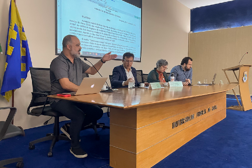 Imagem: Foto mostra o palco do auditório Martins Filho na Reitoria com a mesa onde estão sentados em cadeiras, da esquerda para a direita, o pró-reitor de Assistência Estudantil, Bruno Rocha; o reitor Custódio Almeida; a vice-reitora Diana Azevedo; e o coordenador de Articulação Política institucional da UFC, Daniel Fonsêca.