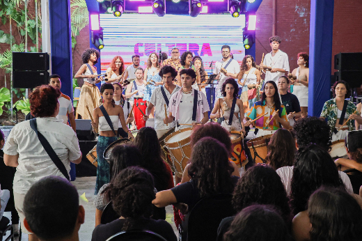 Imagem: estudantes com instrumentos musicais de percussão de apresentam em cima de um palco