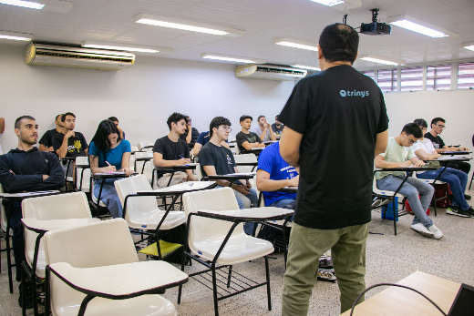 Imagem: Professor de costas em uma sala de aula. Ele veste camisa de malha preta e uma calça verde. A frente dele, estudantes em carteiras escolares (Foto: Ribamar Neto/UFC Informa)