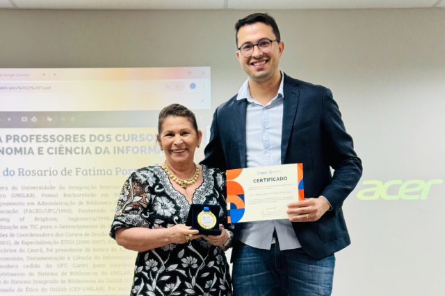 Imagem: mulher segura medalha ao lado de homem que segura certificado