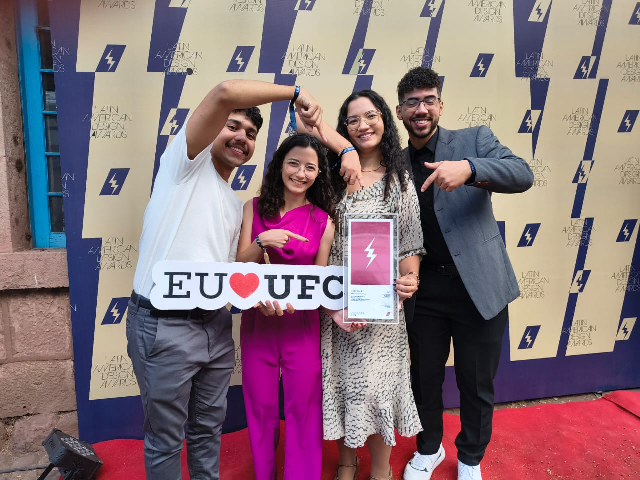 Imagem: Equipe mostra quatro estudantes reunidos (dois homens e duas mulheres) apontando para a placa de premiação. Um dos estudantes segura outra placa, onde se lê:  "Eu amo UFC" 