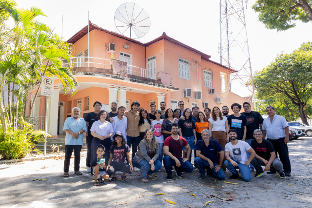 Equipe da Universitária FM reunida na frente da fachada da emissora