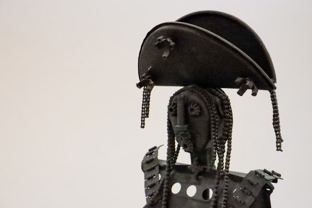 Zé Pinto transforma restos de metal em personagens da memória popular nordestina, como na escultura da Maria Bonita (Foto: Régis Torquato/MAUC) Imagem: Escultura metálica representando uma figura humana com chapéu de cangaceiro. A obra é composta por peças e correntes de ferro reaproveitadas, formando o rosto, os cabelos e o traje. O fundo é neutro, destacando os detalhes e a textura do material.