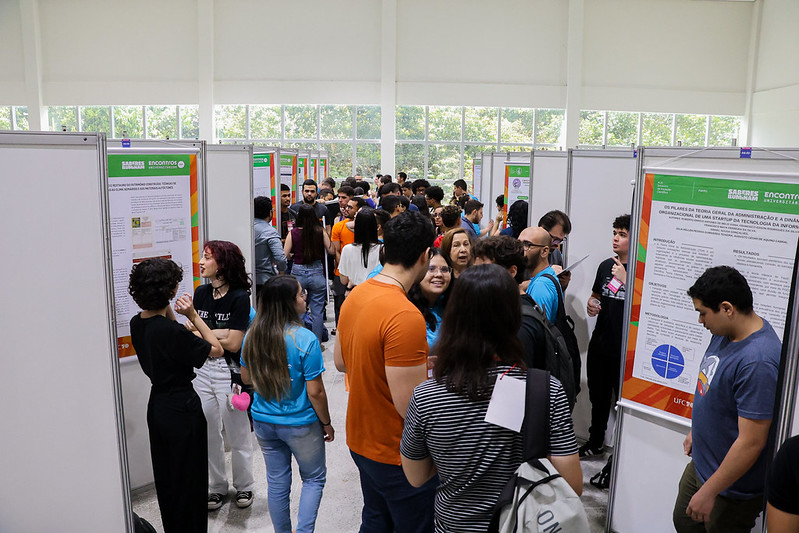 Imagem: foto de vista superior de vários estudantes em um grande salão com totens onde são expostos os banners dos encontros universotários 