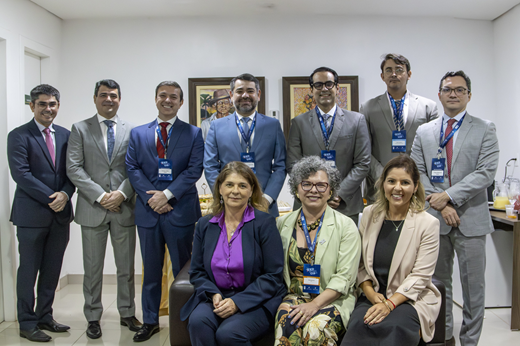Sete homens em pé (todos magistrados) e três mulheres sentadas (duas representantes do PNUD e a vice-reitora da UFC) sorriem em sala na Justiça Federal no Ceará