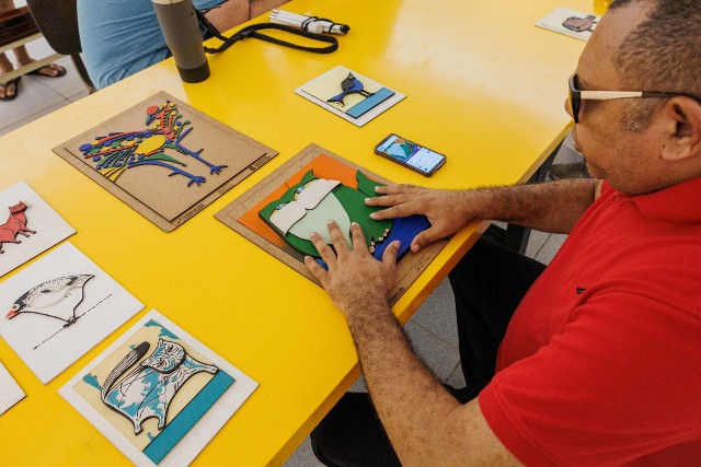 Imagem: Homem fazendo leitura em peça tátil de uma obra de Aldemir Martins 