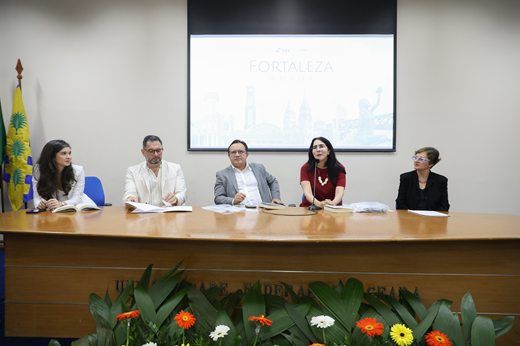 Imagem: Sentados à mesa, no Auditório da Reitoria, estão Juliana Diniz (vice-diretora da Editora UFC), Cavalcante Júnior (diretor da Editora UFC), Custódio Almeida (reitor), Tércia Montenegro (professora do Centro de Humanidades e autora de crônica na obra) e Ana Márcia Diógenes (jornalista e autora de crônica na obra).