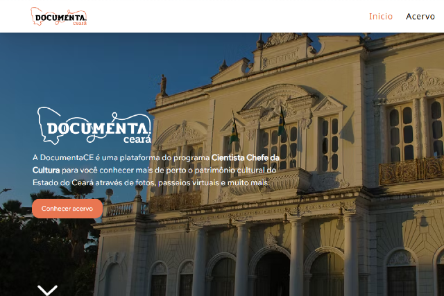 Imagem: Captura de tela de um site com imagem de fundo mostrando a fachada de um prédio histórico em estilo neoclássico, com colunas, janelas ornamentadas e bandeiras hasteadas na sacada central, sob céu azul. No canto superior esquerdo aparece a logomarca “Documenta Ceará”. No canto superior direito, há um menu com as opções “Início” e “Acervo”. Sobre a imagem, à esquerda, lê-se: “DOCUMENTA ceará”. Abaixo, o texto informa: “A DocumentaCE é uma plataforma do programa Cientista Chefe da Cultura para você conhecer mais de perto o patrimônio cultural do Estado do Ceará através de fotos, passeios virtuais e muito mais.” Há também um botão em destaque com a frase “Conhecer acervo”. Na parte inferior, ao centro, aparece um ícone de seta indicando rolagem para baixo.