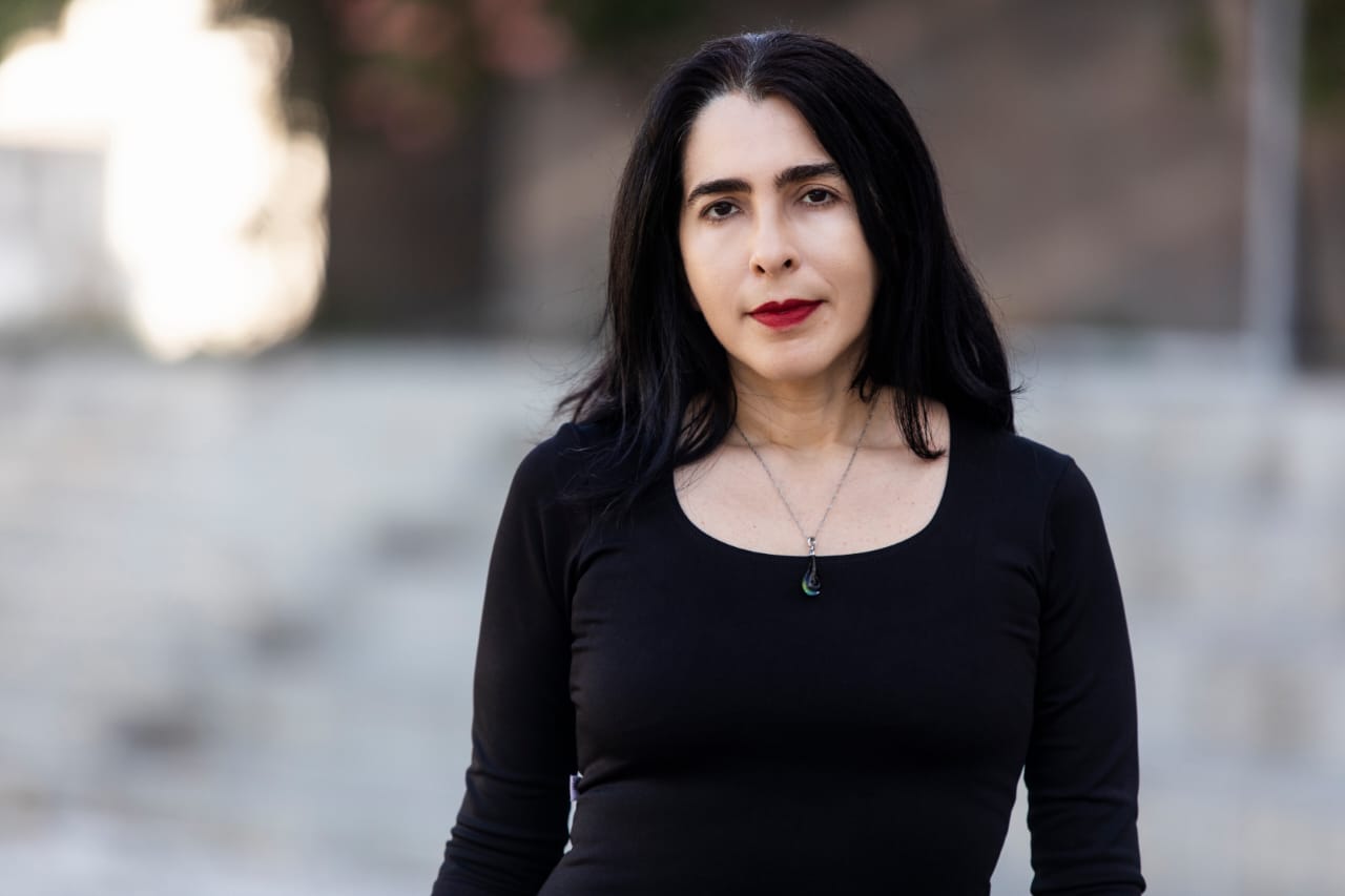 Imagem: foto da professora Tércia Montenegro, autora do livro Dicionário amoroso de Fortaleza, usando camisa preta de mangas longas