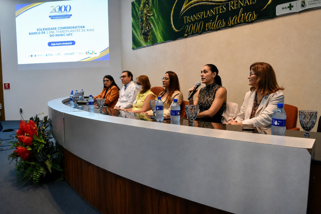 Imagem: mesa de autoridades sentadas em uma mesa em um auditório