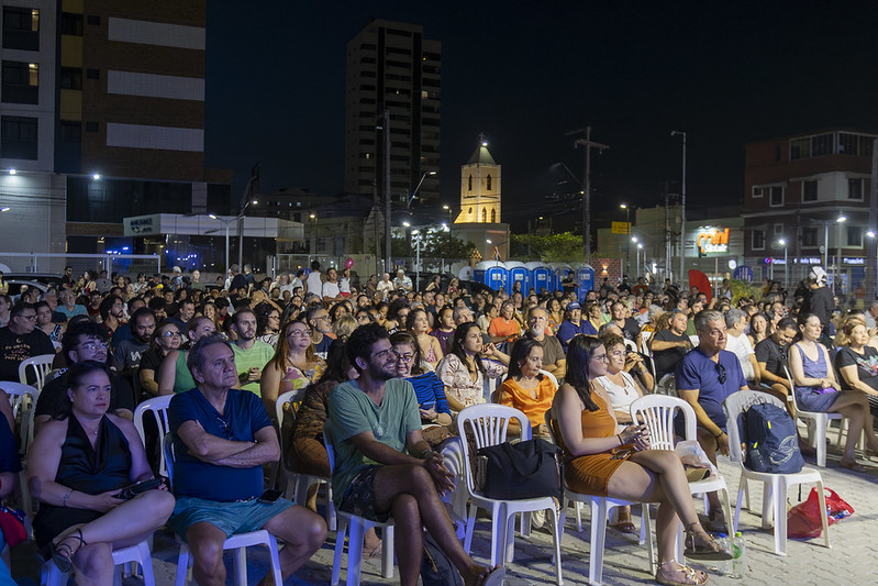 Imagem: plateia presente na inauguração da Praça Cultural São Pedro, na Praia de Iracema, com a Capela de São Pedro iluminada ao fundo